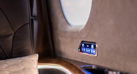 Luxurious private jet interior with a leather seat, quilted cushion, wooden armrest, control panel, window, and cup holder, creating an atmosphere of comfort and elegance.